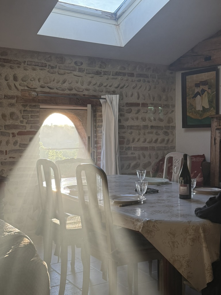 Pièce de vie sous les combles : grande table dressée, murs de galets et porte vitrée en plein cintre