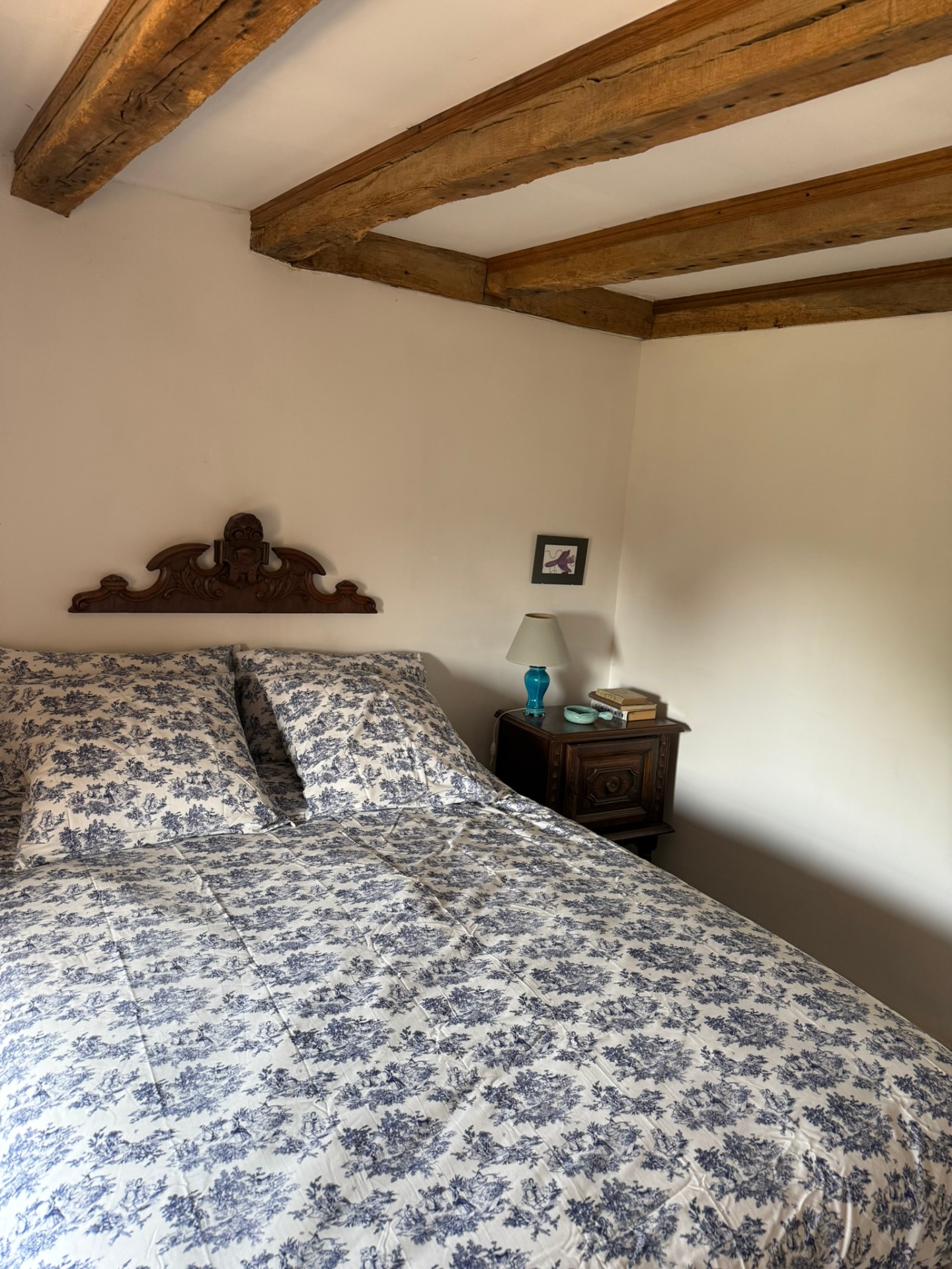 Chambre bleue : mur de galets, poutres anciennes et lit au chevet sculpté