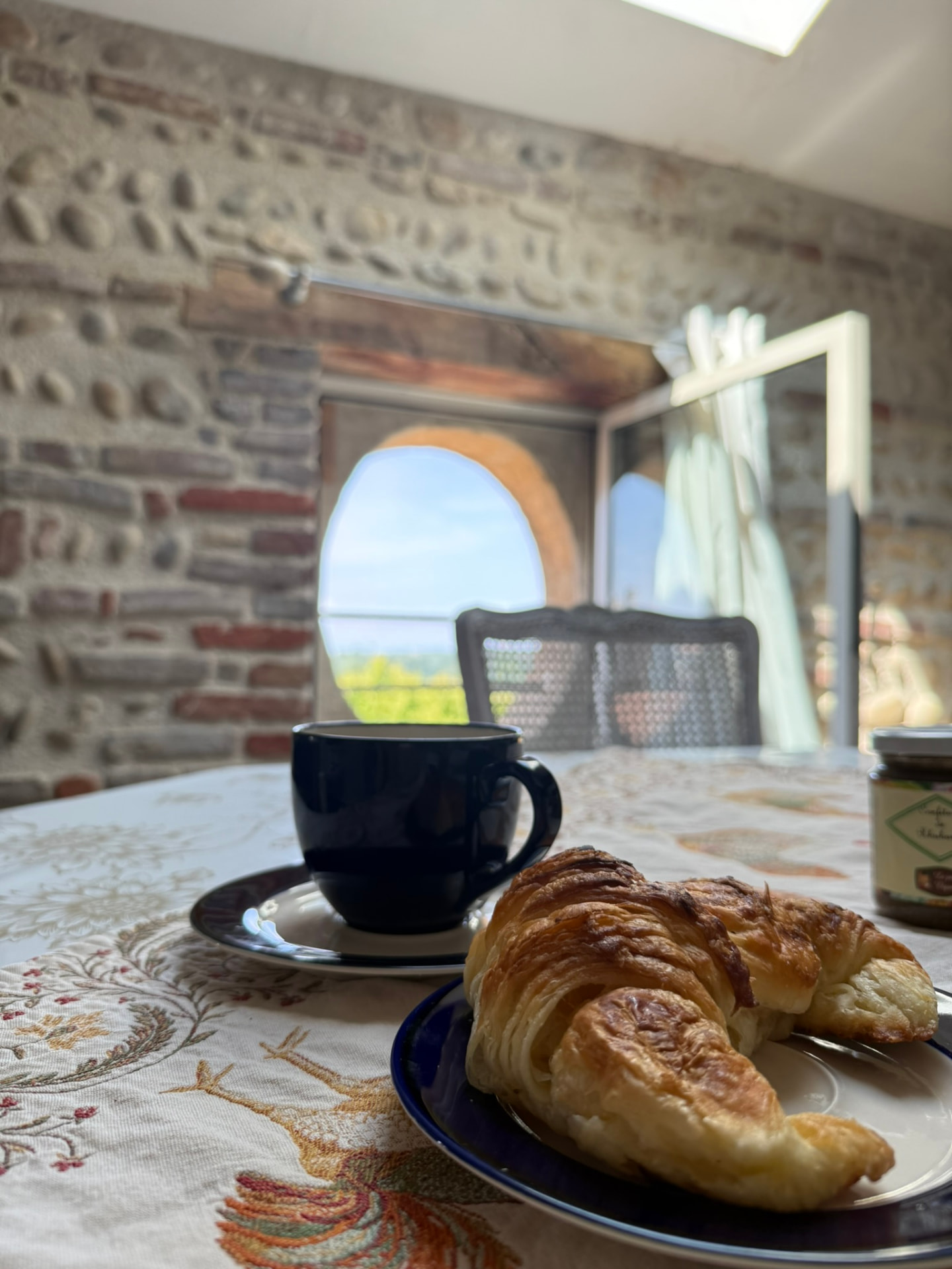 Café et croissant sur la table du salon, lumière du velux et mur de galets