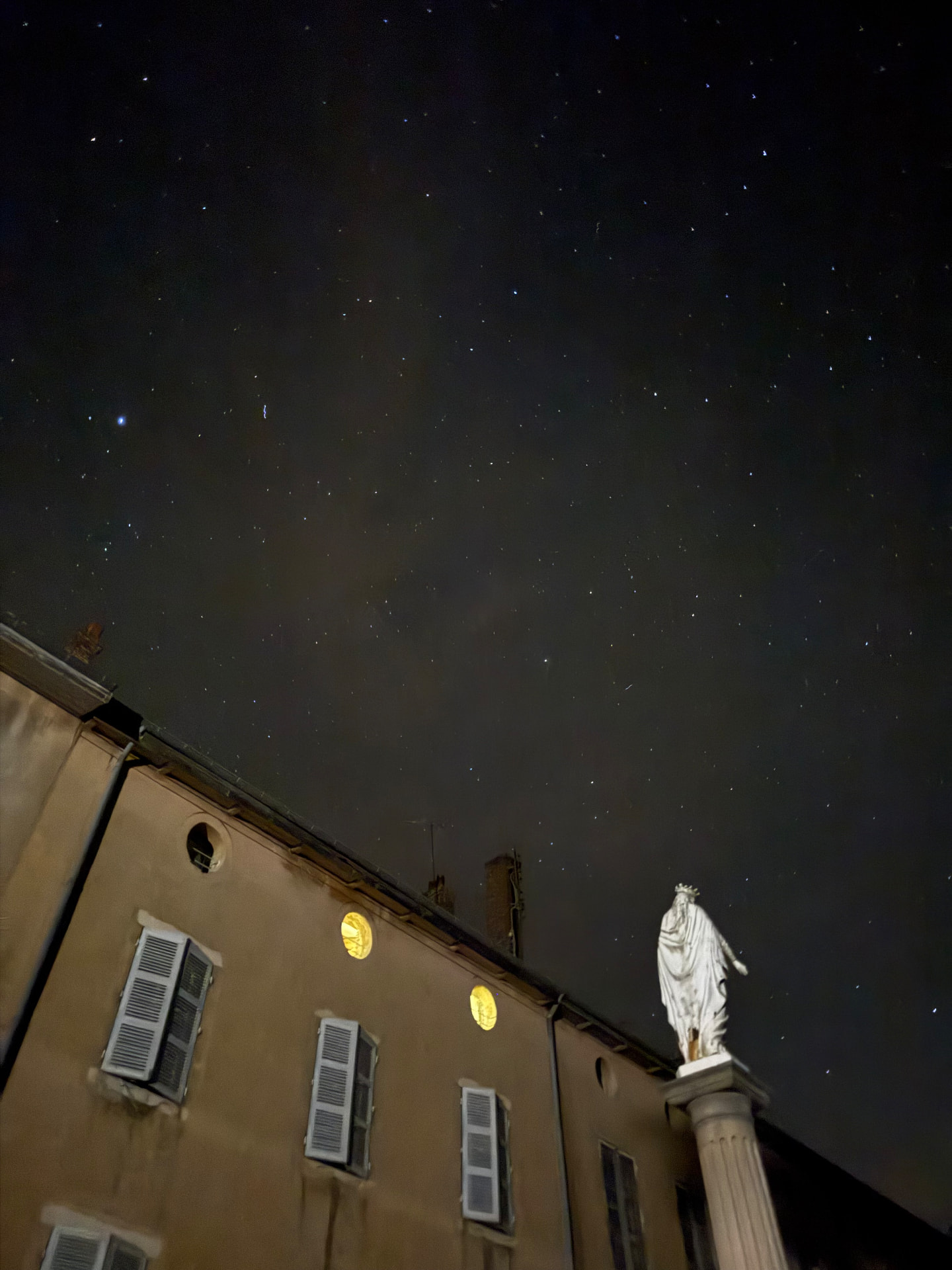 La statue et la façade du château de Neuville-les-Dames sous un ciel étoilé