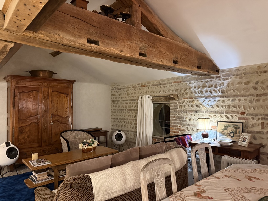 Vue du salon avec poutres massives, mur de galets et coin lecture