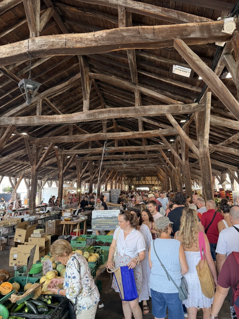 La foule du marché sous la charpente de chêne des halles