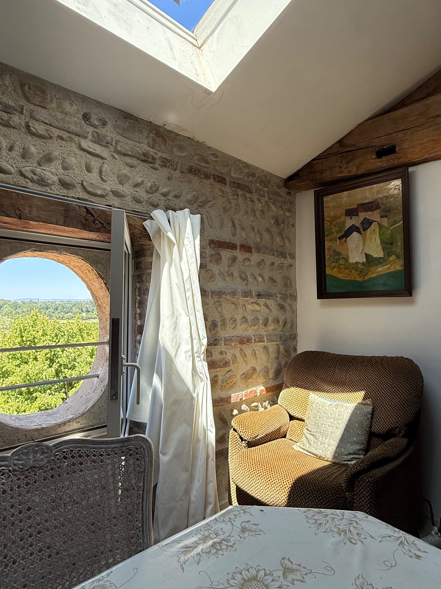 Coin salon sous verrière avec fauteuil et fenêtre ronde donnant sur la campagne