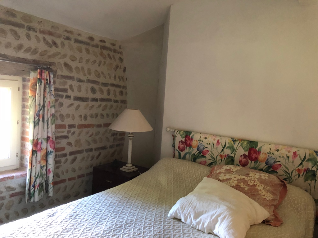 Le mur de galets et briques et la fenêtre aux rideaux fleuris de la chambre du château