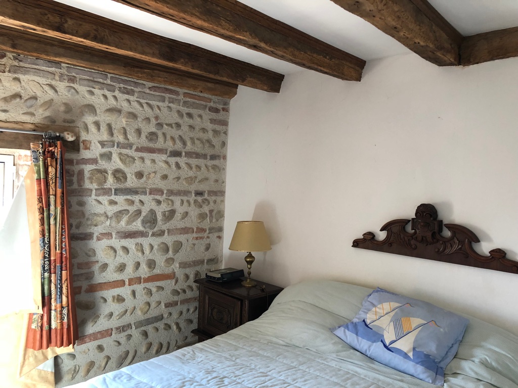 Chambre bleue : mur de galets, poutres anciennes et lit au chevet sculpté